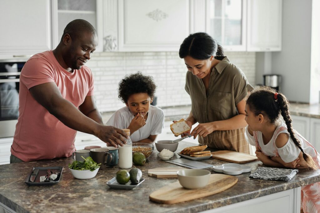 Mom and dad preparing breakfast together, with their kids standing by their side in the kitchen.